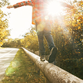 Person balancing on a guardrail, arms outstretched, with sunlight streaming through trees on a quiet rural road.