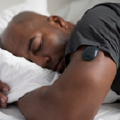 A person lies asleep in bed, wearing a Eversense CGM on their upper arm in a bright bedroom.